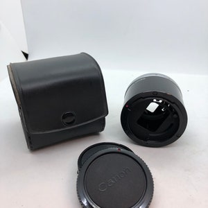 May include: A black Canon lens adapter with a black leather case and a black lens cap.