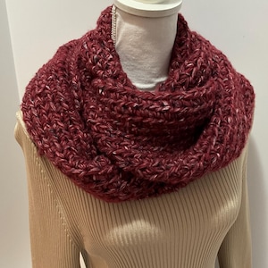 May include: A burgundy knitted infinity scarf with a textured pattern. The scarf is displayed on a mannequin wearing a beige sweater.