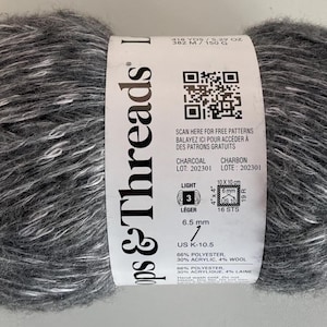 May include: A ball of charcoal gray yarn with white flecks, labeled "Loops & Threads." The label includes a QR code, the word "Charcoal," and measurements. The yarn is 6.5 mm and US K-10.5.