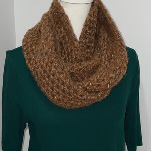 May include: A brown knitted infinity scarf with a textured pattern. The scarf is displayed on a mannequin wearing a dark green shirt.