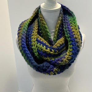 May include: A chunky knit infinity scarf in shades of blue, green, and purple. The scarf is made with a thick yarn and has a textured stitch pattern.