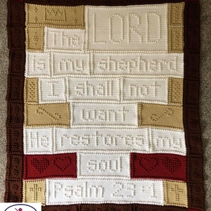 Può includere: Una coperta all'uncinetto bianca con le parole "The Lord is my shepherd, I shall not want, He restores my soul, Psalm 23" in filato marrone e beige. La coperta ha un bordo marrone con cuori rossi.