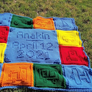 May include: A blue crocheted baby blanket with a personalized name and birthdate, "Anakin - April 12, 2021", in the center. The blanket is made up of colorful squares with different designs, including a sailboat, a truck, a house, and a ball.