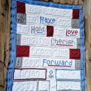 Puede incluir: Una manta de crochet blanca con borde azul y cuadrados rojos y grises. La manta tiene el texto "To Have and To Hold to Love and to Cherish from this day Forward" y "Julie 2016" en blanco.