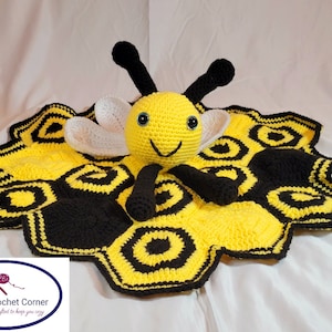 May include: A crocheted bee-themed baby blanket with a yellow and black honeycomb pattern. A crocheted bee with white wings is attached to the center of the blanket.