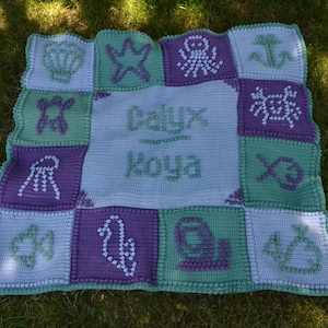 Puede incluir: Una manta de bebé de crochet con un fondo azul claro y cuadrados morados y verdes. Cada cuadrado presenta una criatura marina diferente, incluyendo una estrella de mar, un pulpo, una concha, una tortuga, un pez y un ancla. La manta está personalizada con el nombre "Cayux Koya".