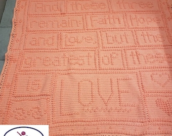 May include: A peach-colored crocheted blanket with the words "And This Is Our Family" and "Love" in a raised stitch pattern. The blanket is bordered with a crocheted edging. The text "Julie's Crochet Corner" and "Hooked by: Teri Clouser" are in the bottom left corner.