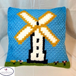 May include: A blue crocheted pillow with a white and yellow windmill design. The pillow has a green border and small yellow flowers.