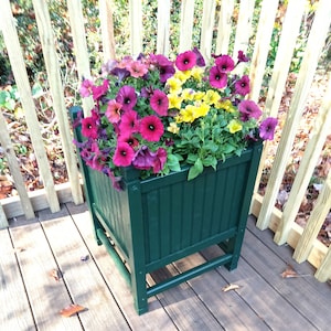Puede incluir: Una jardinera de madera verde con una variedad de flores rosas, moradas y amarillas. La jardinera está sentada en una terraza de madera.