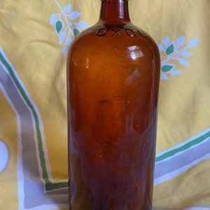 Könnte beinhalten: Eine dunkelbraune Glasflasche mit abgerundetem Boden und schmalem Hals. Die Flasche hat ein Etikett mit dem aufgedruckten Wort "OXOL".