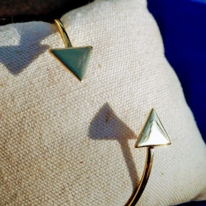 Può includere: Due braccialetti rigidi in oro con estremità triangolari. I triangoli sono di colore blu chiaro e hanno una finitura lucida.