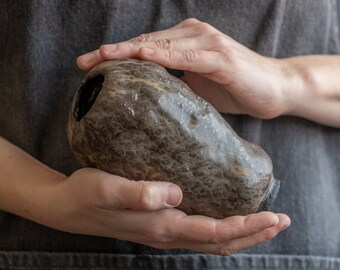 May include: A person is holding a brown and black ceramic vase with a textured surface.