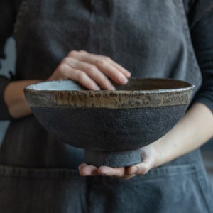 Pode incluir: Uma tigela grande de cerâmica preta com uma borda marrom. A tigela tem uma superfície texturizada e uma base larga e redonda.