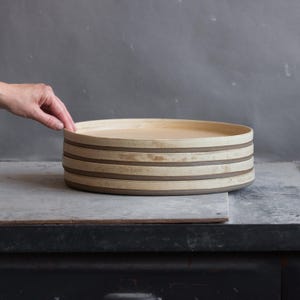 Puede incluir: Una pila de cuatro platos redondos de cerámica con un interior de color crema y un exterior gris oscuro. Los platos presentan una base plana y un borde ligeramente elevado, mostrando un acabado texturizado y terroso en los laterales.
