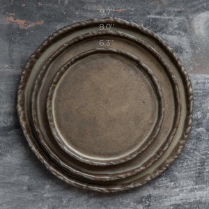 Może przedstawiać: Trzy ceramiczne talerze włożone w siebie, z brązową glazurą. Talerze mają średnicę 16 cm, 20 cm i 25 cm.