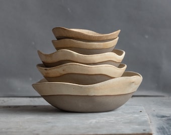 May include: A set of four ceramic bowls with a wavy rim and a light brown glaze. The bowls are stacked on top of each other, with the largest bowl at the bottom and the smallest bowl at the top.
