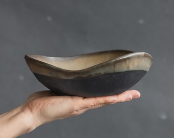May include: A black and brown ceramic bowl with a wavy rim. The bowl is being held in a hand.