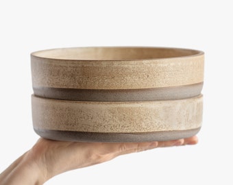 May include: Two stacked ceramic bowls with a speckled beige glaze and a brown rim.