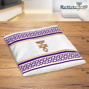 K&ouml;nnte beinhalten: Ein wei&szlig;er Tallit mit violetten und goldenen Streifen und einem Davidstern mit einem Menora-Design. Der Tallit liegt auf einer Holzoberfl&auml;che.