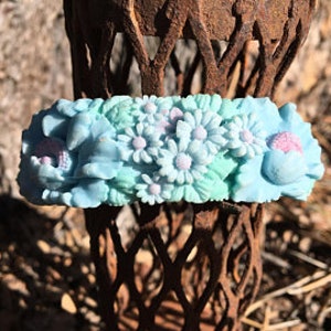 May include: A light blue floral headband with white and pink flowers. The headband is made of polymer clay and is handmade.