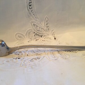 May include: A silver candle snuffer with a long, curved handle. The snuffer has a rounded, spoon-like end for extinguishing candles.