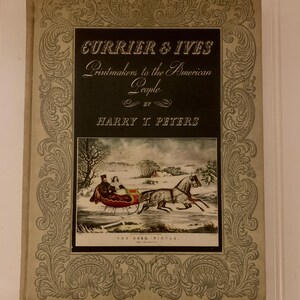 May include: A vintage book titled "Currier & Ives Printmakers to the American People" by Harry T. Peters. The cover features an illustration of a horse-drawn sleigh in a winter scene, framed by an ornate border. The book's cover is a light beige color.
