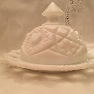 May include: A white milk glass butter dish with a domed lid and a scalloped edge. The lid has a raised, geometric design.