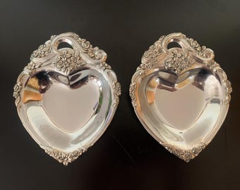 May include: Two silver heart-shaped serving dishes with ornate floral designs and handles.