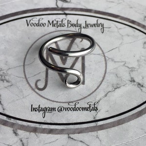 May include: Silver body jewellery in the shape of a double spiral. The jewellery is on a white background with the text "Voodoo Metals Body Jewellery" and "Instagram @voodoometals".
