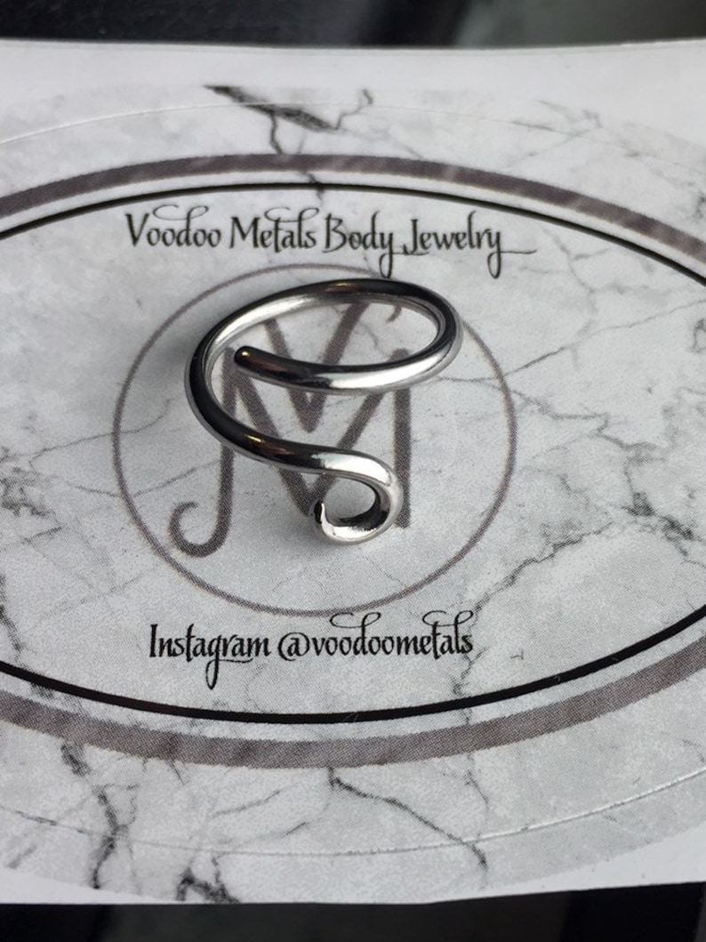 May include: Silver body jewellery in the shape of a double spiral. The jewellery is on a white background with the text "Voodoo Metals Body Jewellery" and "Instagram @voodoometals".
