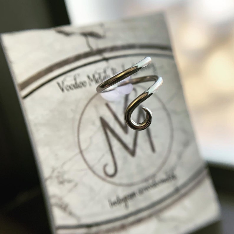 May include: Silver ear cuff with a spiral design. The cuff is made of wire and is designed to be worn on the upper part of the ear.