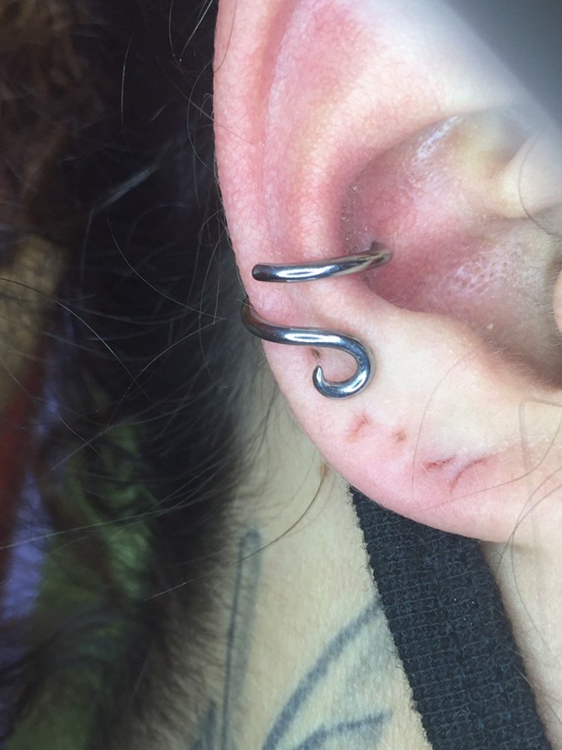 May include: A silver ear cuff with a curved design. The cuff is worn in the upper ear, near the helix.