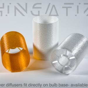 May include: Three cylindrical bulb cover diffusers in the image. One is orange, one is white, and one is silver. The orange diffuser is on its side, while the white one stands upright. The silver diffuser is on its side, showing its base.