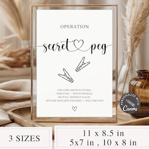 Puede incluir: Una impresión enmarcada en blanco con las palabras "Operation Secret Peg" en escritura negra. La impresión incluye dos ilustraciones de pinzas de ropa y el texto "Clip a peg and play it cool..." El marco es dorado y la impresión está disponible en 3 tamaños: 27,9 x 21,6 cm, 12,7 x 17,8 cm y 25,4 x 20,3 cm.