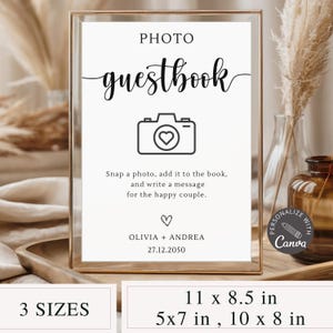 Puede incluir: Un letrero de libro de visitas con foto enmarcado con el texto "PHOTO guestbook" en escritura elegante. El letrero incluye un gráfico de cámara con un corazón e instrucciones para agregar una foto y un mensaje. Disponible en 3 tamaños: 27,9 x 21,6 cm, 12,7 x 17,8 cm y 25,4 x 20,3 cm.