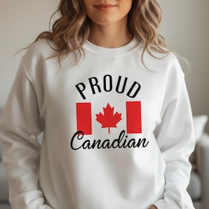 Könnte beinhalten: Weißes Sweatshirt mit dem Text "PROUD Canadian" in schwarzer Schrift und einem roten Ahornblatt-Design. Das Ahornblatt ist in einem roten Rechteck zentriert, ein Symbol Kanadas. Das Sweatshirt ist ein lässiger Stil.