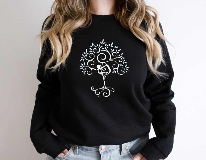 May include: Black sweatshirt with a white tree design. The tree features a person in a yoga pose within the branches. The design includes leaves and swirling patterns, creating a unique and artistic look. A comfortable and stylish top.