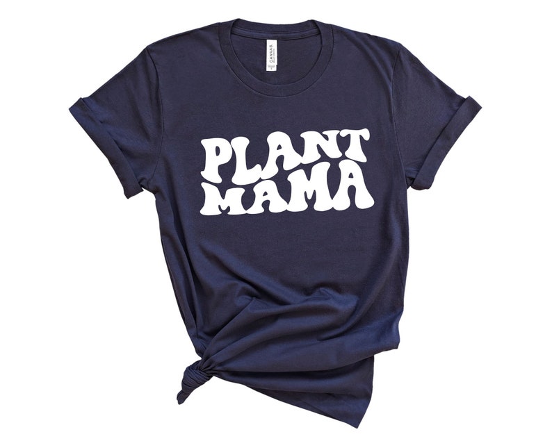 K&ouml;nnte beinhalten: Marineblaues T-Shirt mit dem wei&szlig;en Text "PLANT MAMA" in einem Retro-Schriftstil. Das Shirt ist am Saum geknotet und hat hochgekrempelte &Auml;rmel. Das T-Shirt besteht aus einem weichen Material.