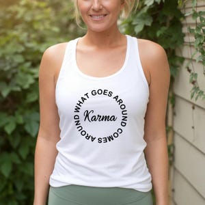May include: White tank top with the text "Karma" in a circular design. The text "WHAT GOES AROUND COMES AROUND" surrounds the word "Karma". The tank top is sleeveless and has a scoop neck.