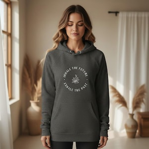 May include: A charcoal gray hoodie with a front pocket and a drawstring hood. The hoodie features a white circular graphic with the text "INHALE THE FUTURE, EXHALE THE PAST" surrounding a lotus flower design. The model is wearing the hoodie.