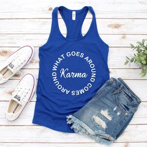 May include: A royal blue racerback tank top with the words "WHAT GOES AROUND COMES AROUND Karma" in a white circular design. The tank top is paired with denim shorts and white sneakers.