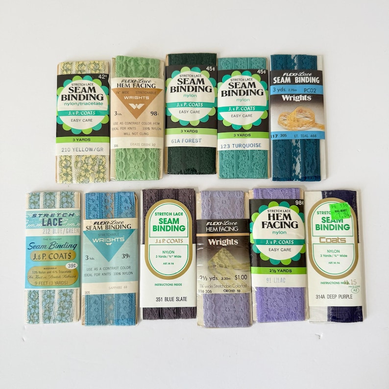 May include: A collection of vintage seam binding and hem facing rolls in various colors, including yellow, green, blue, and purple. Each roll is labeled with the brand "J&P Coats" or "Wrights" and includes yardage information.