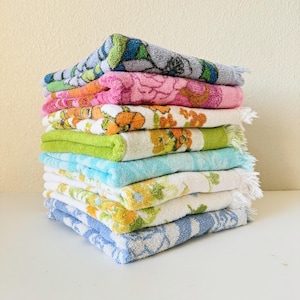 May include: A stack of ten folded rectangular cotton towels featuring various patterns and colours including blue, pink, orange, lime green, light blue, yellow, and white. Each towel has a textured terry cloth surface with fringed edges.