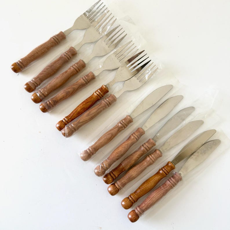 K&ouml;nnte beinhalten: Ein Set aus Edelstahlgabeln und -messern mit Holzgriffen. Die Gabeln haben vier Zinken, und die Messer haben eine glatte Klinge. Die Holzgriffe sind in verschiedenen Braunt&ouml;nen gehalten.