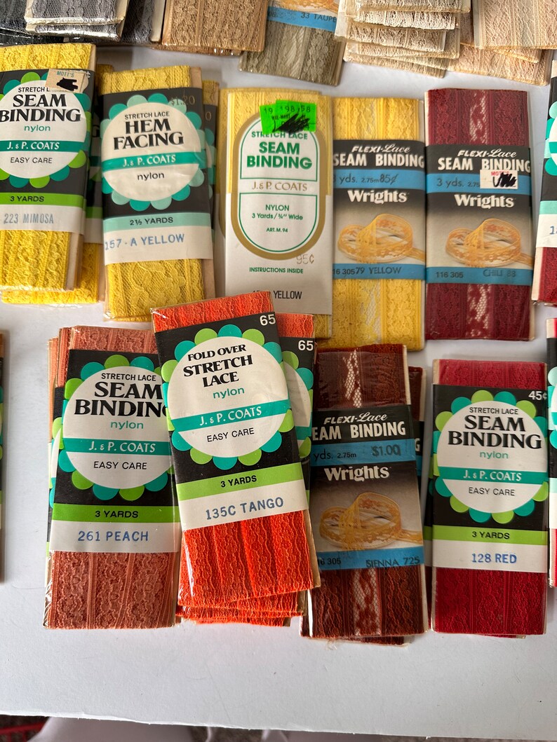 May include: A collection of vintage seam binding and hem facing rolls in various colors. The packages display text such as "Stretch Lace Seam Binding" and "J. & P. Coats." Colors include yellow, peach, red, and orange. Each roll is labeled with the yardage.