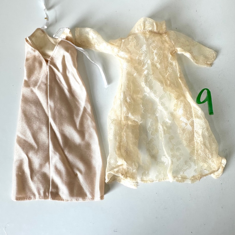 Op de afbeelding: Twee beige jurken, een is effen en de andere is een transparante kanten overlay.