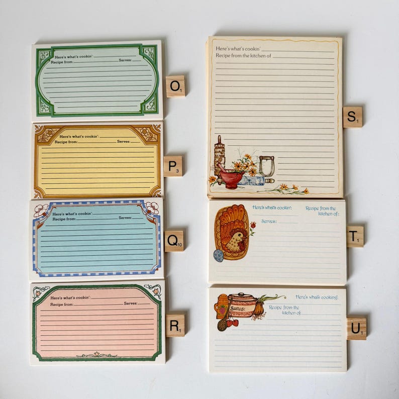 May include: A collection of vintage recipe cards in various colors, including green, yellow, blue, and pink. Each card features lined spaces for recipe details and decorative borders. Some cards have illustrations of kitchen items and text that reads "Here's what's cookin".