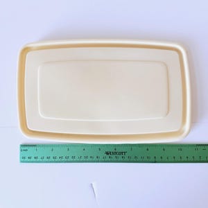 May include: A rectangular, off-white plastic lid with a raised center panel. A green Westcott ruler is positioned along the bottom edge, showing the lid measures approximately 11.5 inches in length and 6 inches in width.