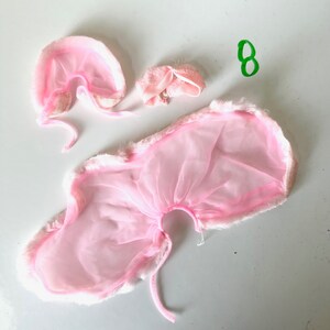 Op de afbeelding: Roze nep bont en tule kostuumset met een cape, capuchon en een klein bijpassend accessoire. De set is perfect voor een fee of engel kostuum.