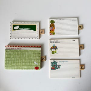 May include: A collection of recipe cards with various designs and text. One card features a sheep illustration and the text "From my kitchen with love...". Other cards have fruit, floral, and kitchen-themed illustrations. Each card has lined spaces for recipe details.